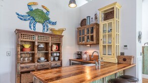 A kitchen with wooden cabinets, a large island with stools, and a decorative crab wall art piece. - Cedar Bluff Cabin in May in Old Town Bluffton on the river (Bluffton)