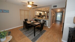 A dining area with a table and chairs, a ceiling fan, and a kitchen in the background. - Beautiful Ponce Inlet 2bd Condo.  100 Yards to the Beach! Beach supplies/bikes.  (Ponce Inlet)