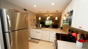 A modern kitchen with stainless steel appliances, white cabinetry, and a dining area visible through the window. - Beautiful Ponce Inlet 2bd Condo.  100 Yards to the Beach! Beach supplies/bikes.  (Ponce Inlet)