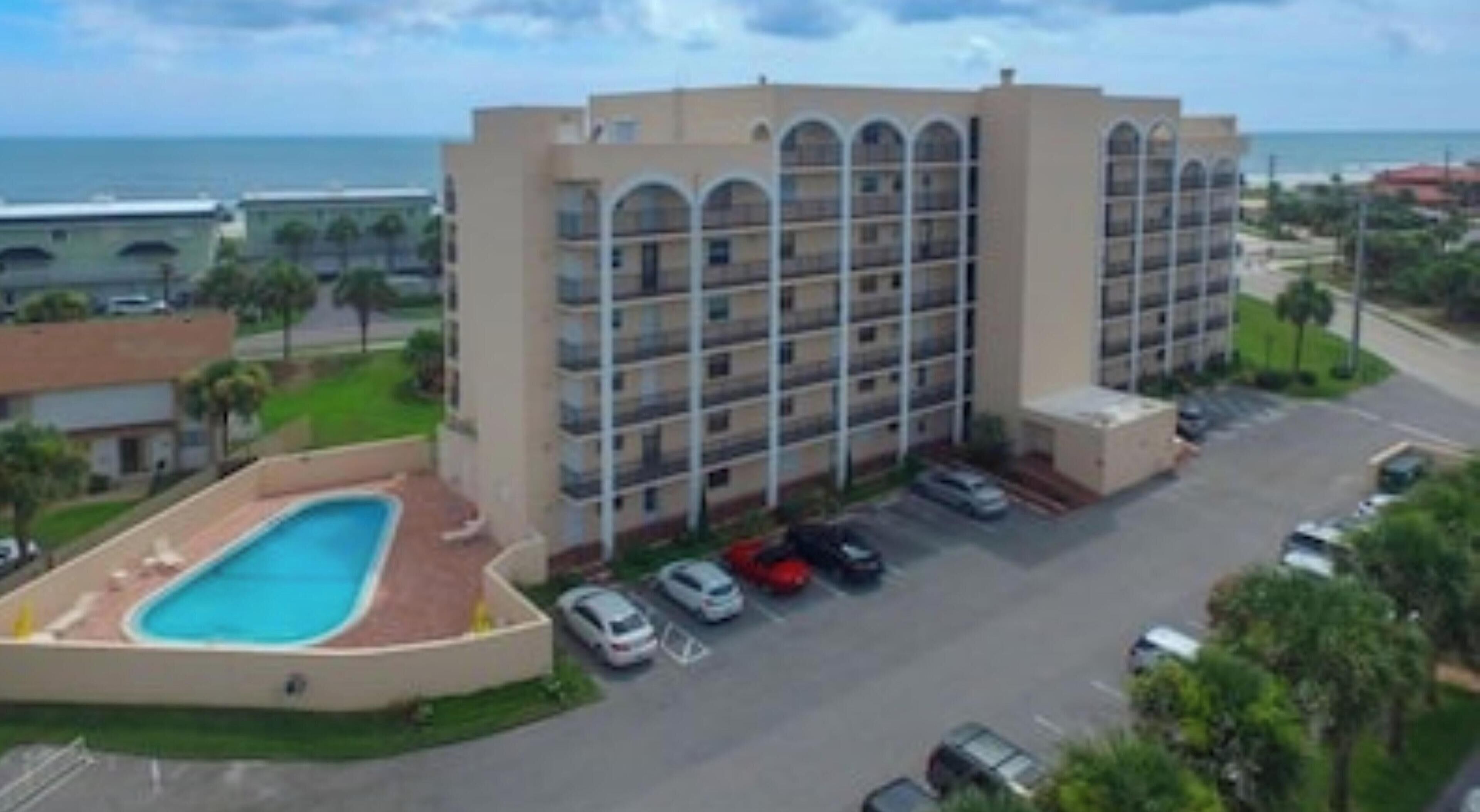 A multi-story hotel with a swimming pool and a parking lot.