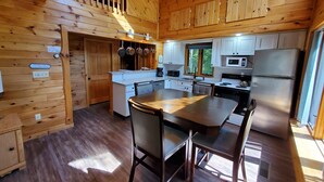 A wooden cabin-style kitchen with a central island, white cabinets, and a dining area with chairs. - Peace and quiet on the lake (Becket)