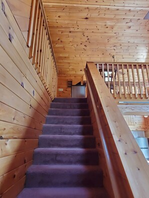 Stairs lead to an upper level, flanked by railings and surrounded by wooden walls and ceiling.