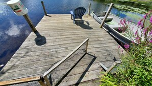 A wooden dock extending into a calm river, with a chair and a boat docked nearby. - Peace and quiet on the lake (Becket)
