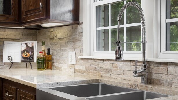 Una cocina con un lavamanos doble de acero inoxidable, armarios de madera, un protector contra salpicaduras de piedra y una ventana con vistas a la vegetación.