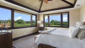 Un dormitorio amplio con una cama grande, dos mesitas de noche, una silla y vista a un campo de golf.