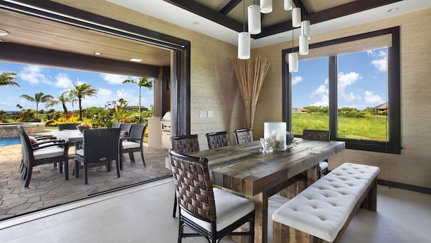 Un espacio habitable integrado con una mesa de comedor de madera, sillas de mimbre, un banco y vistas a un jardín exuberante y una piscina.