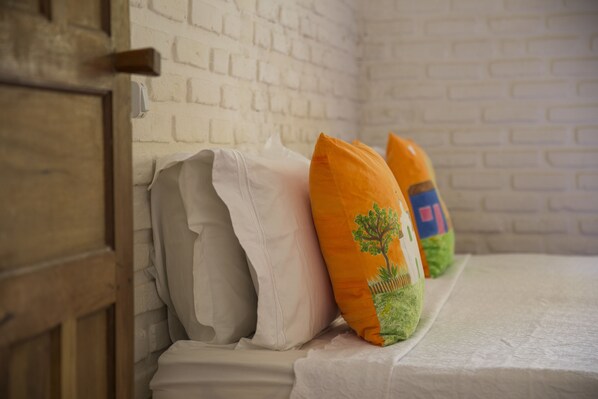 Una cama con ropa blanca y almohadas decorativas frente a una pared de ladrillo blanco.