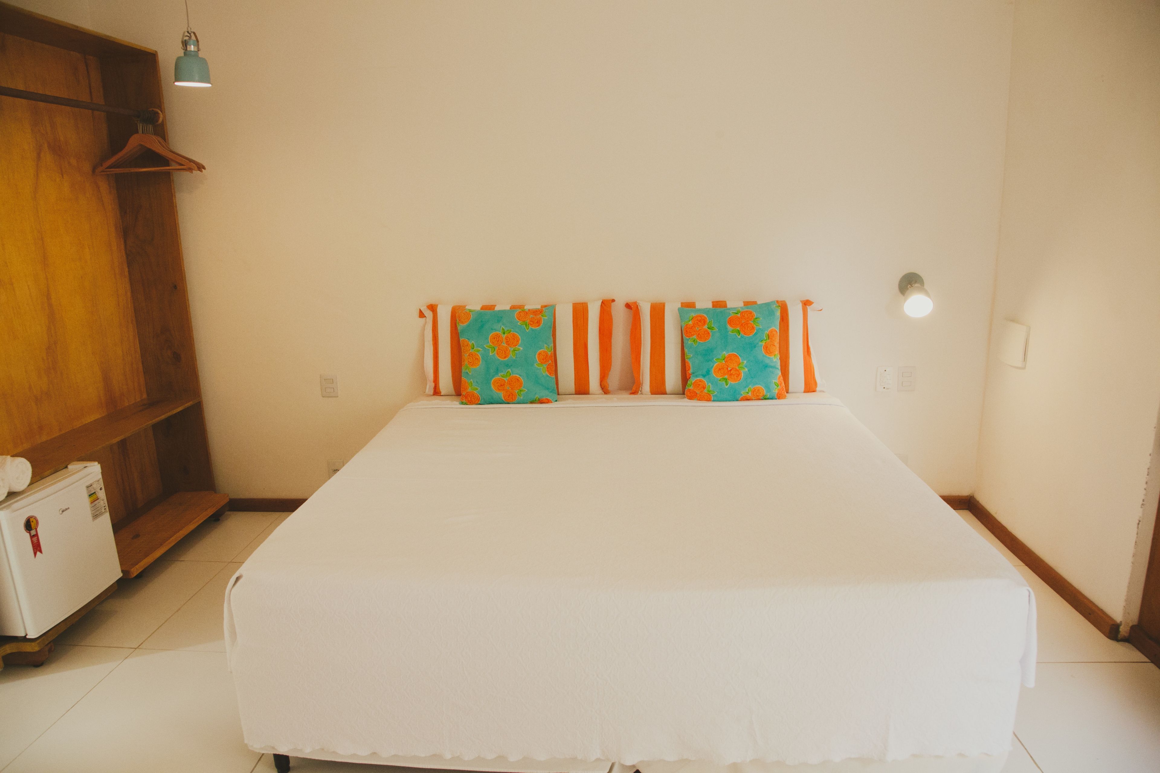 Un dormitorio con una cama, un armario de madera, una lámpara colgante y un pequeño electrodoméstico blanco.