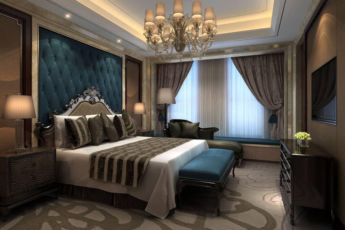 A luxurious bedroom with a tufted headboard, a large bed, an ottoman, a desk, and a TV.