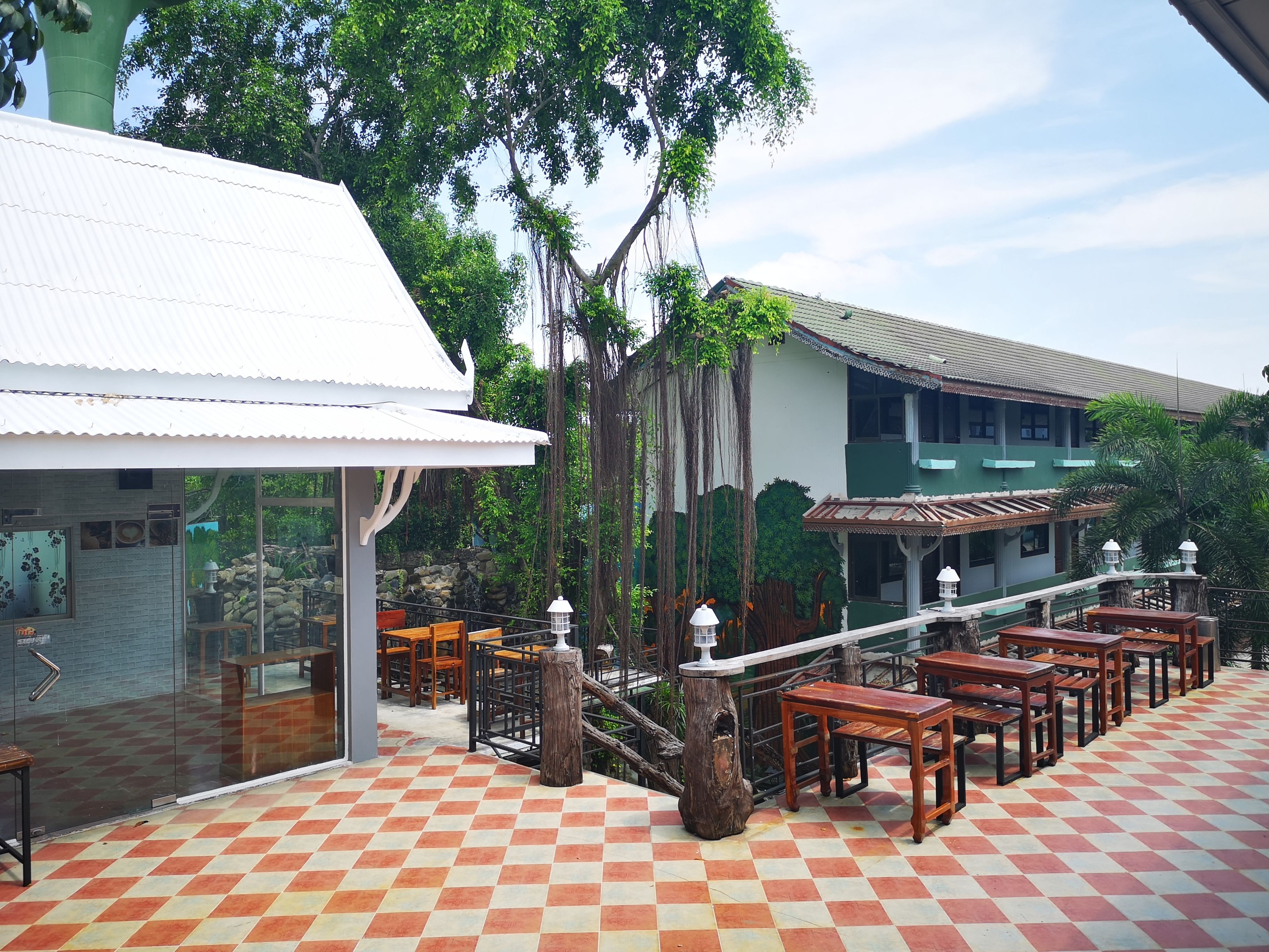 A restaurant with outdoor seating, a checkered floor, and a building with a green roof in the background.