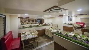 Un restaurante con varias zonas de comedor, una cocina al fondo y una decoración de plantas.