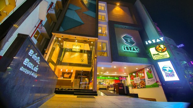 Un edificio de varios pisos con un letrero llamativo de 'iSTAY' y un restaurante llamado 'iSTAY Chetinadu Virundhu' en la planta baja.
