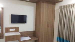 Un dormitorio con un armario de madera, un televisor de pantalla plana en la pared, una mesita de noche y una pequeña mesa redonda.