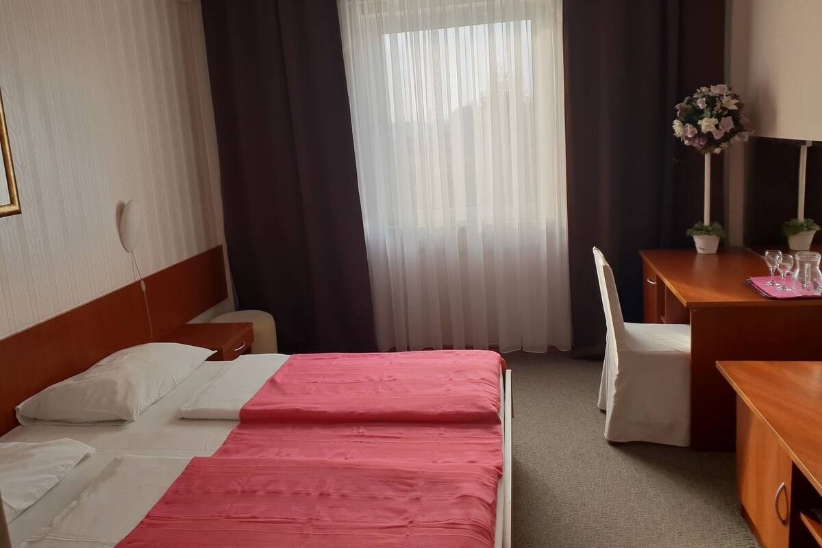 Une chambre d’hôtel avec un lit, un bureau, une chaise et une fenêtre avec des rideaux.