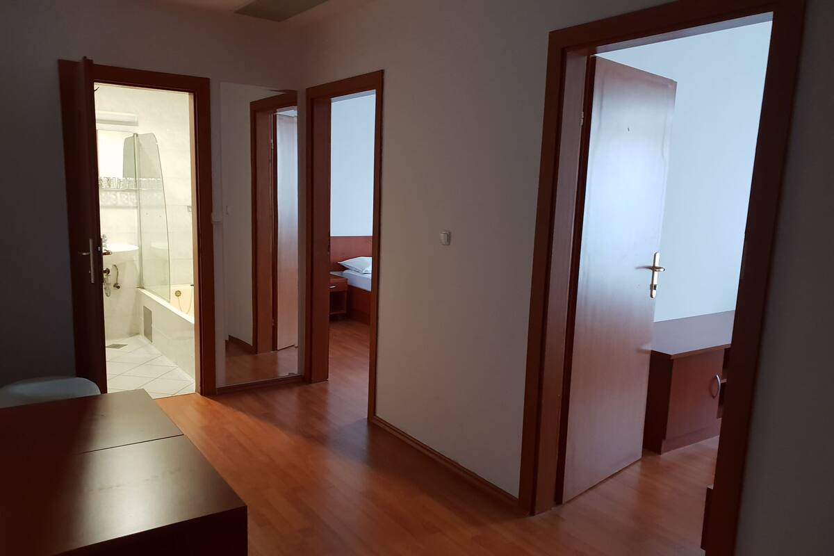 Une pièce spacieuse dotée d’un plancher en bois, d’une grande fenêtre et d’une porte donnant sur une salle de bain avec une douche en verre.