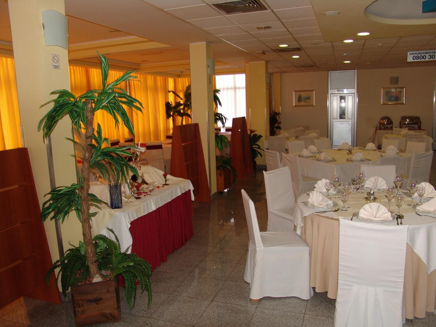 A banquet hall with tables set for dining, chairs, and potted plants.