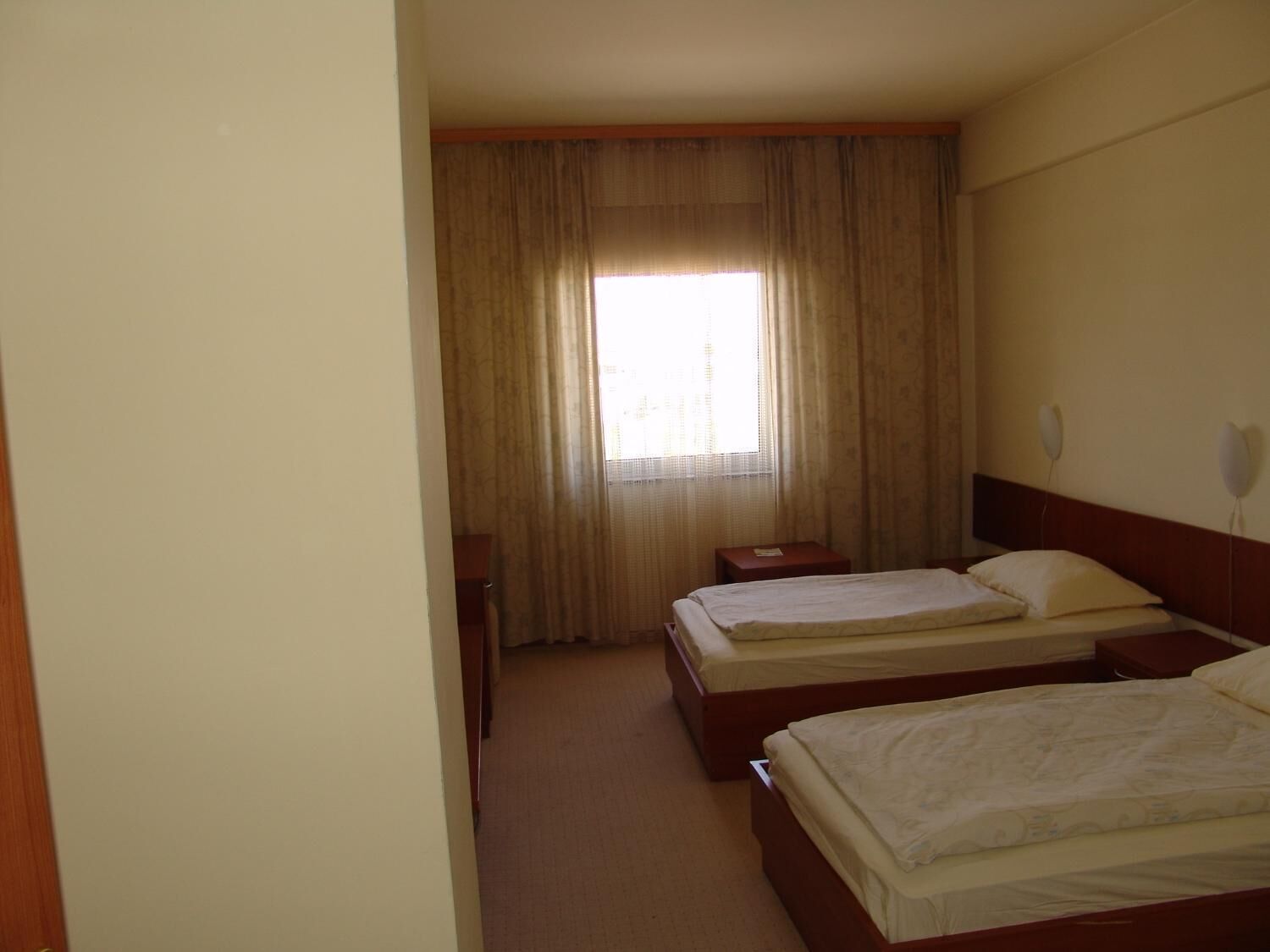 Habitación de hotel con dos camas, una ventana con cortinas, una mesita de noche y un teléfono instalado en la pared.