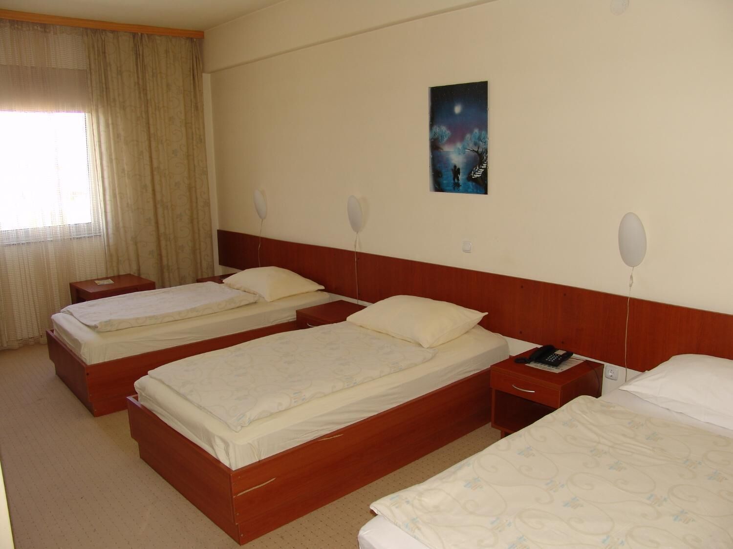 Een hotelkamer met twee enkele bedden, een nachtkastje met een telefoon en een schilderij aan de muur.