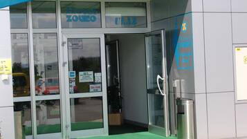 A hotel entrance with glass doors, a blue awning, and a trash bin outside.