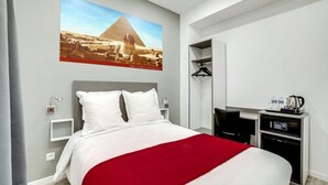 A hotel room with a large bed, a desk with a coffee machine, and a wall-mounted TV. - Paris hôtel (Clichy)