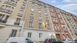 A multi-story residential building with balconies, a white car parked in front, and a clear sky. - Paris hôtel (Clichy)