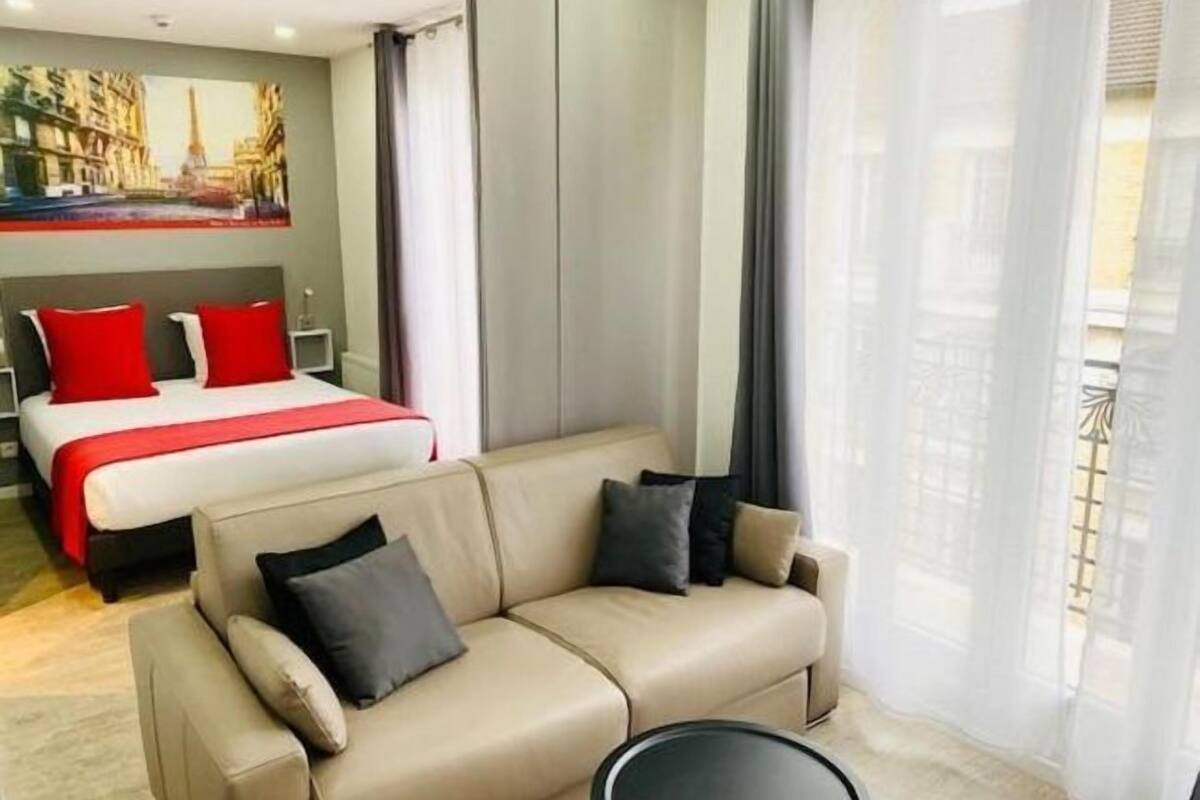 Habitación de hotel con cama, sofá, una mesita y un cuadro de un paisaje urbano en la pared.