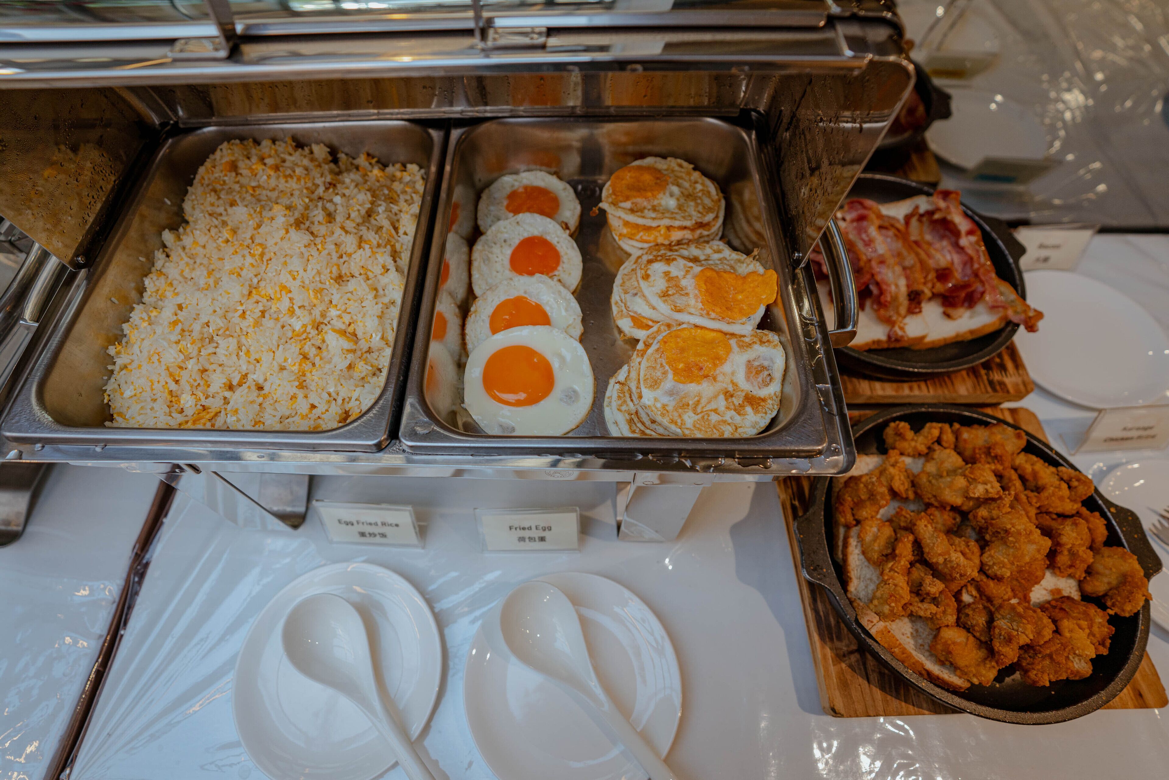 A buffet with various food options including fried eggs, rice, and fried chicken.