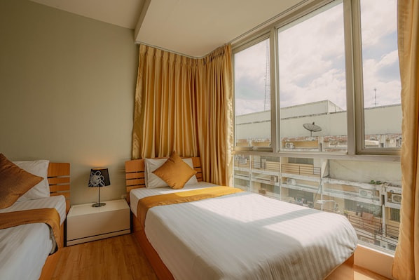 Une chambre d’hôtel avec deux lits, une table de chevet avec une lampe, une grande fenêtre avec des rideaux et une vue sur le paysage urbain.