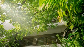 Un edificio de varios niveles con un balcón y abundante follaje verde.