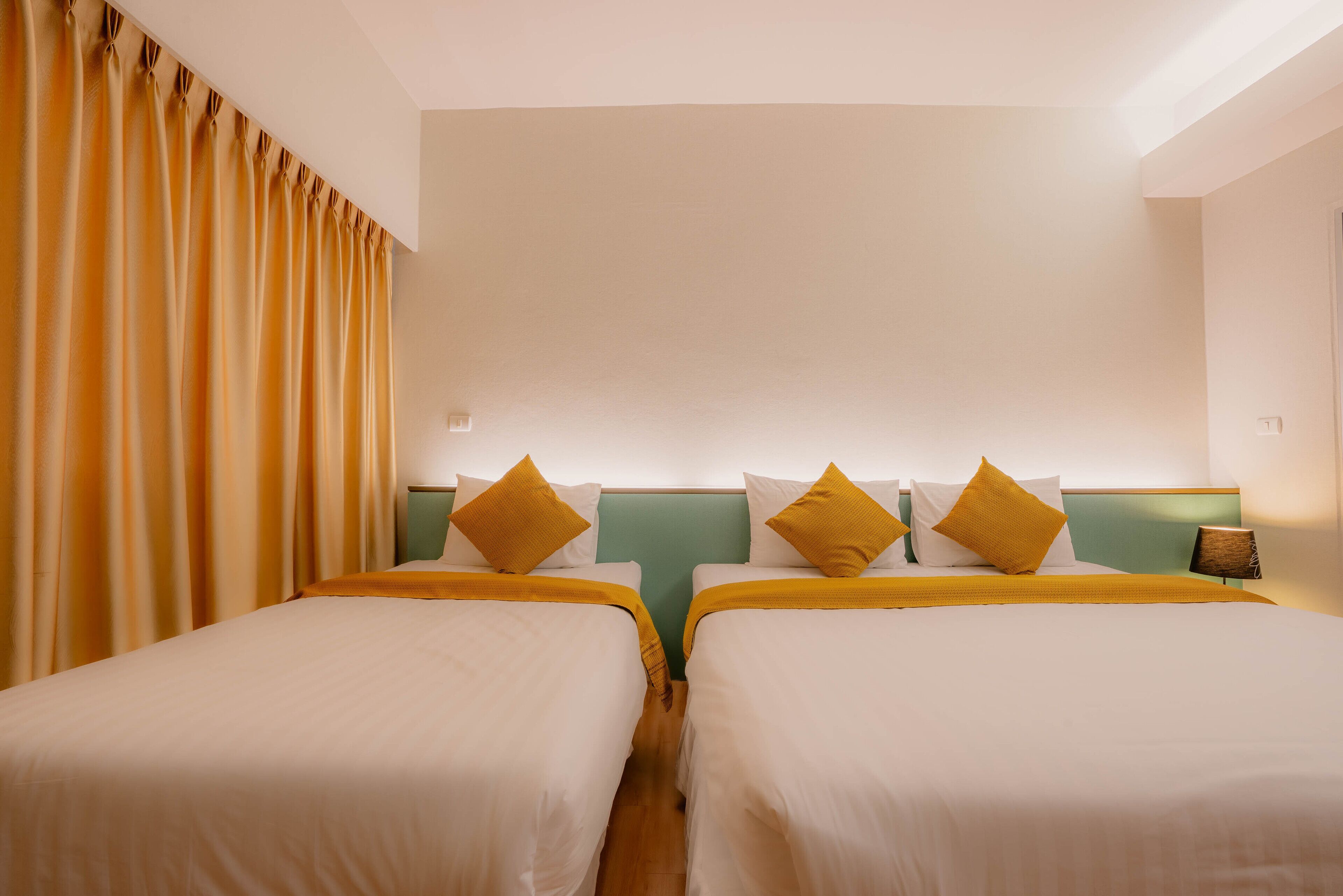 A hotel room with two beds, a green headboard, and a yellow curtain.