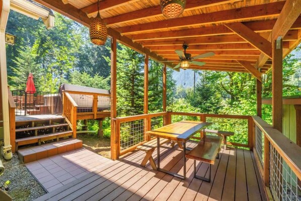 A wooden deck with a table and chairs, surrounded by a wooden railing, and a view of a forested area.