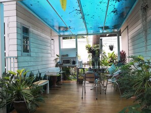 Une terrasse couverte avec un plancher en bois, une table, des chaises et diverses plantes en pot.