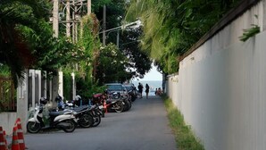 A narrow street lined with parked motorcycles and scooters, a white wall on one side, and a view of the sea in the distance. - Reera Resort (Hua Hin)