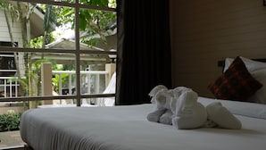 A neatly made bed with white towels, a wooden headboard, and a view of a balcony with plants and a railing. - Reera Resort (Hua Hin)