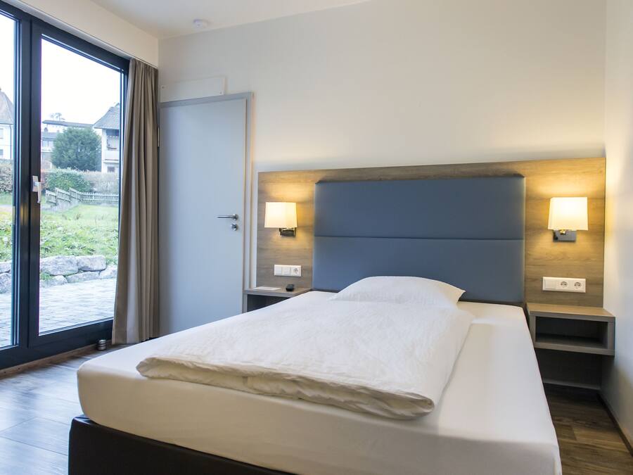A modern hotel room with a large bed, wooden flooring, and a view through a glass door.