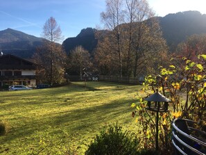 Ein grünes Rasenstück mit einer Laube, einem Holzzaun und einem Berg im Hintergrund.