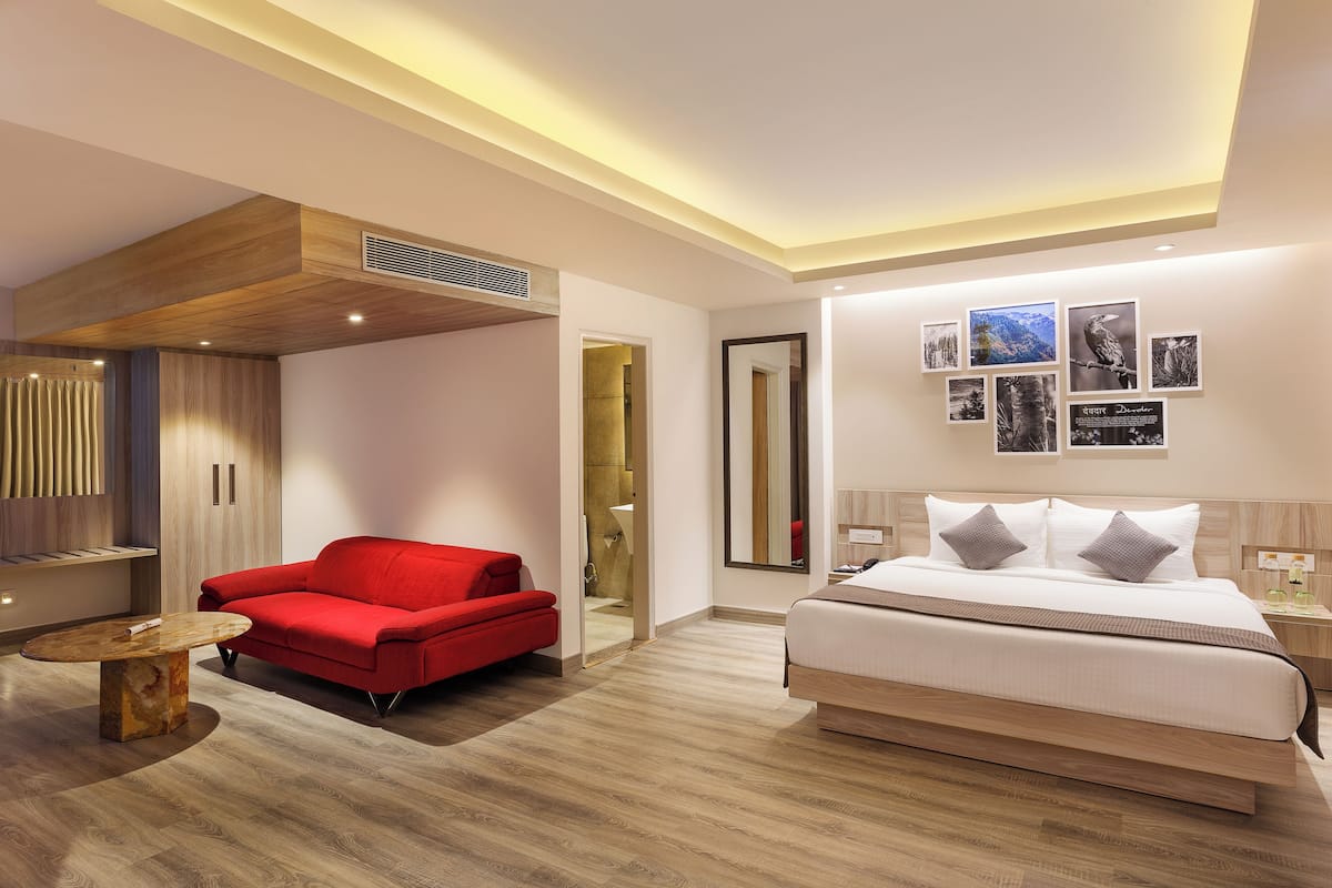 Habitación de hotel moderna con una cama grande, un sofá rojo y un techo de madera.