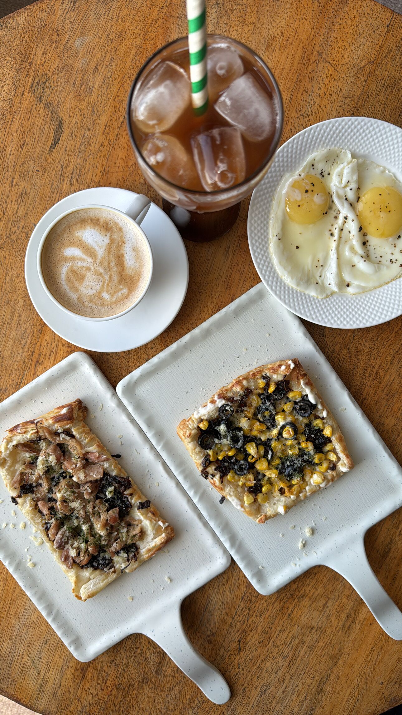 A table with a glass of iced coffee, two plates of food, and a cup of coffee.