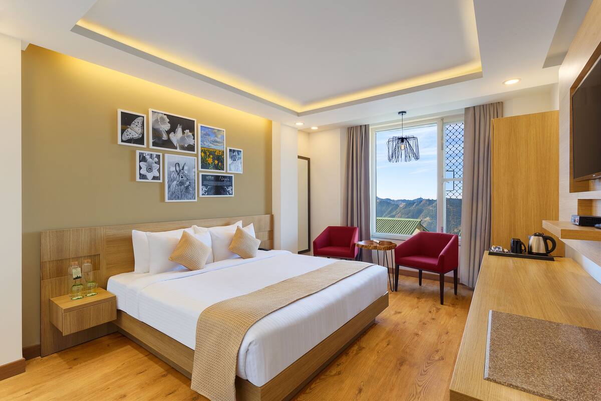 Habitación de hotel con una cama grande, un escritorio con cafetera, una silla roja y obras de arte en la pared.