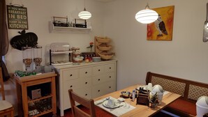 En matplats med ett träbord dukat för två personer, en buffé med olika rätter och ett köksområde med en skylt på väggen.