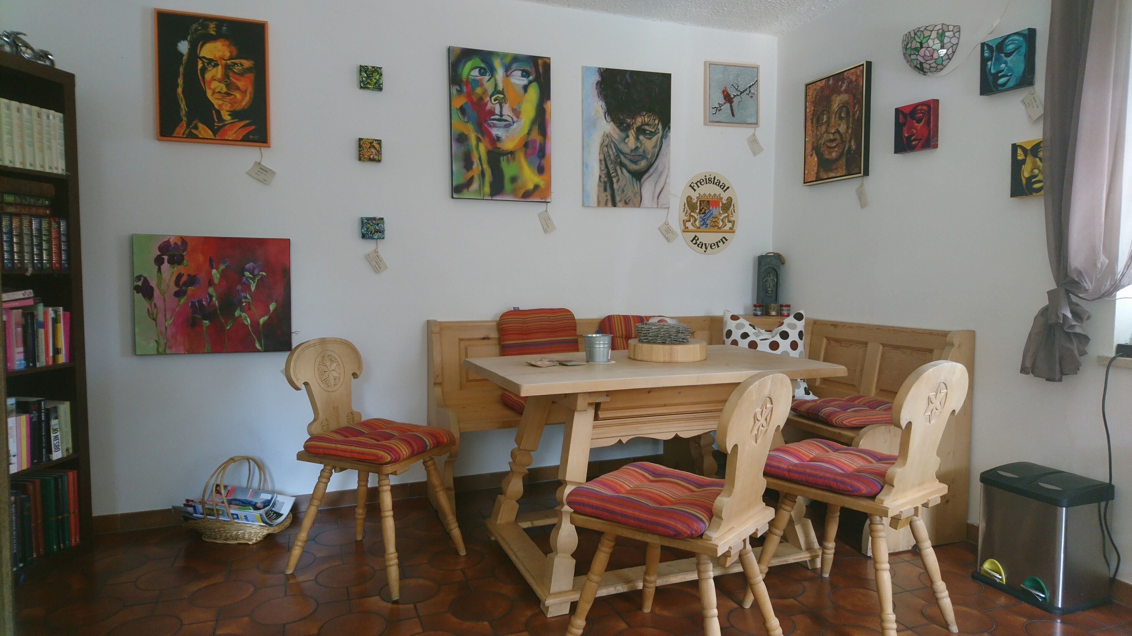 A dining area with a wooden table and chairs, surrounded by various artworks on the walls.