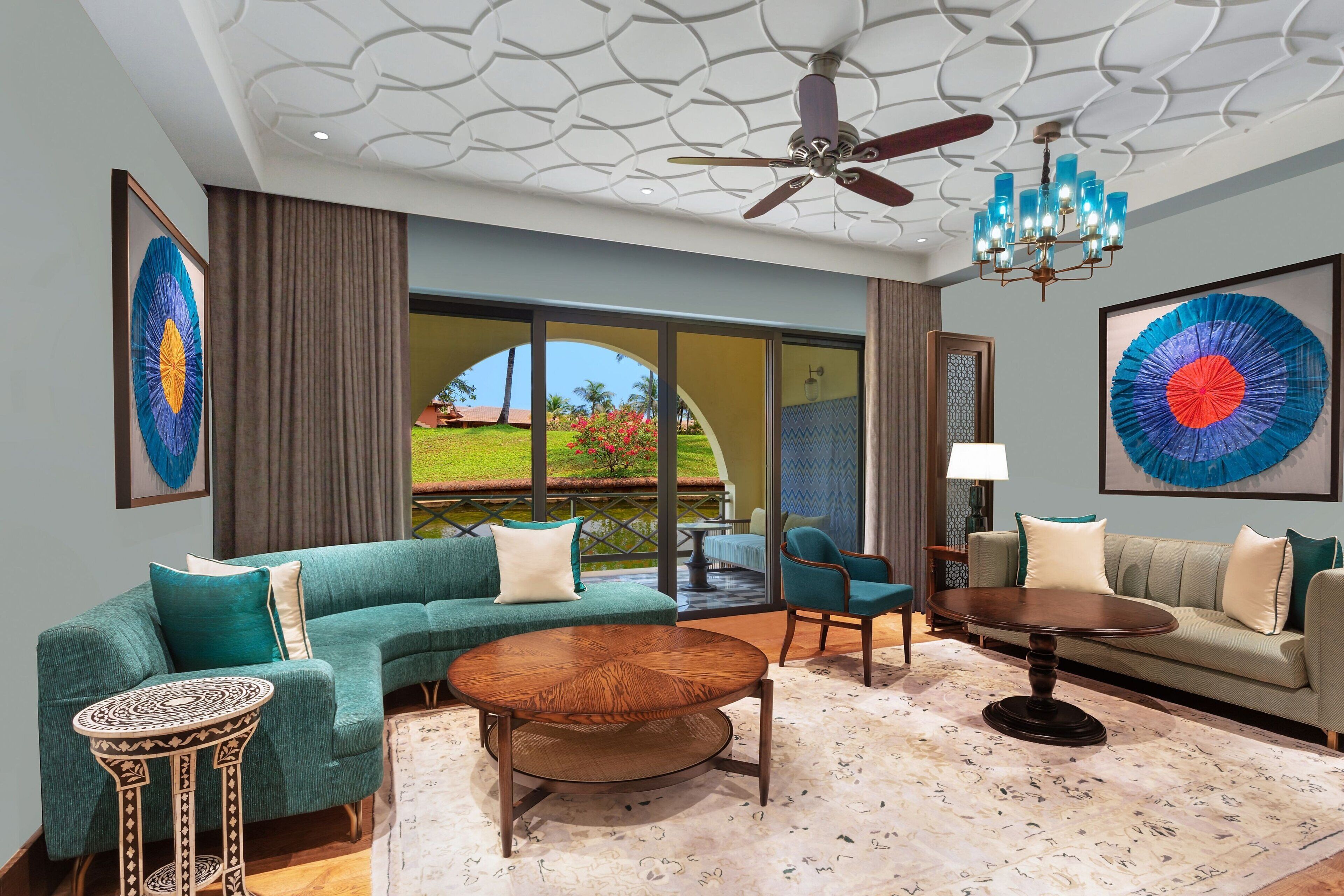 A spacious living area with a green sofa, a round wooden coffee table, and a blue armchair. There is a ceiling fan and a chandelier.
