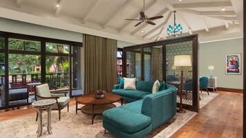 A modern living room with a teal sofa, a round coffee table, and a patterned side table. A ceiling fan and a chandelier are visible.