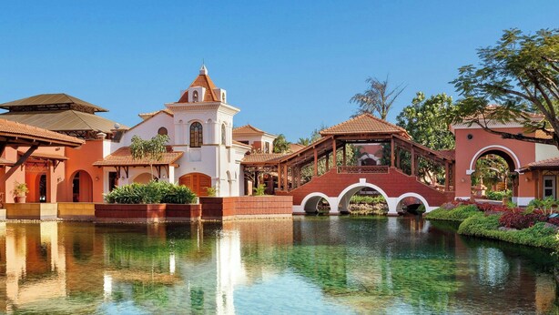 A clear water body reflecting buildings with arched bridges and a central tower. - ITC Grand Goa, a Luxury Collection Resort & Spa, Goa (Cansaulim)