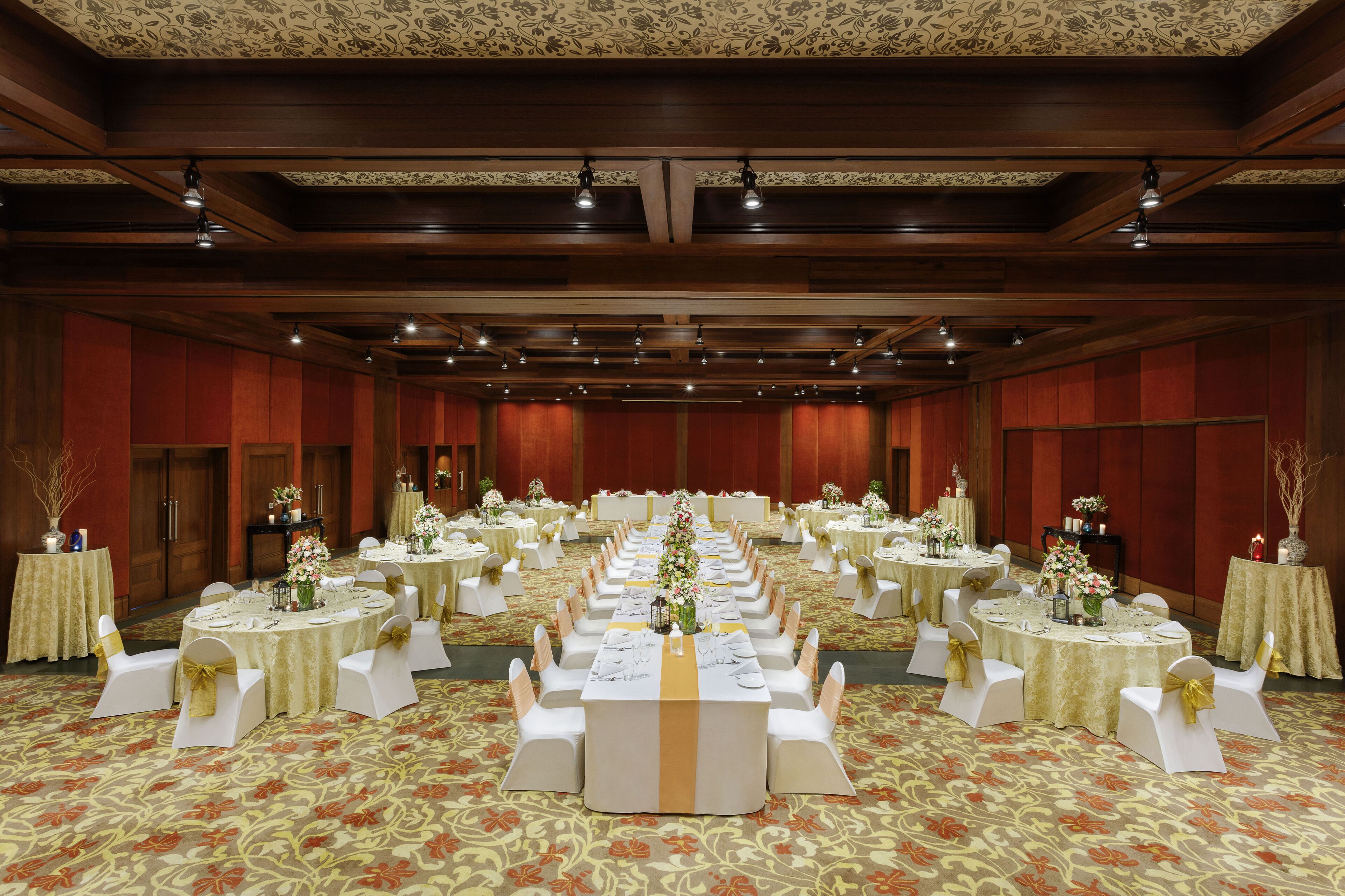 Une salle de banquet dotée de nombreuses tables rondes, chacune recouverte d’une nappe blanche et ornée d’un ruban doré, et entourée de chaises blanches également agrémentées de rubans dorés.