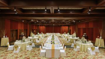 Une salle de banquet dotée de nombreuses tables rondes, chacune recouverte d’une nappe blanche et ornée d’un ruban doré, et entourée de chaises blanches également agrémentées de rubans dorés.