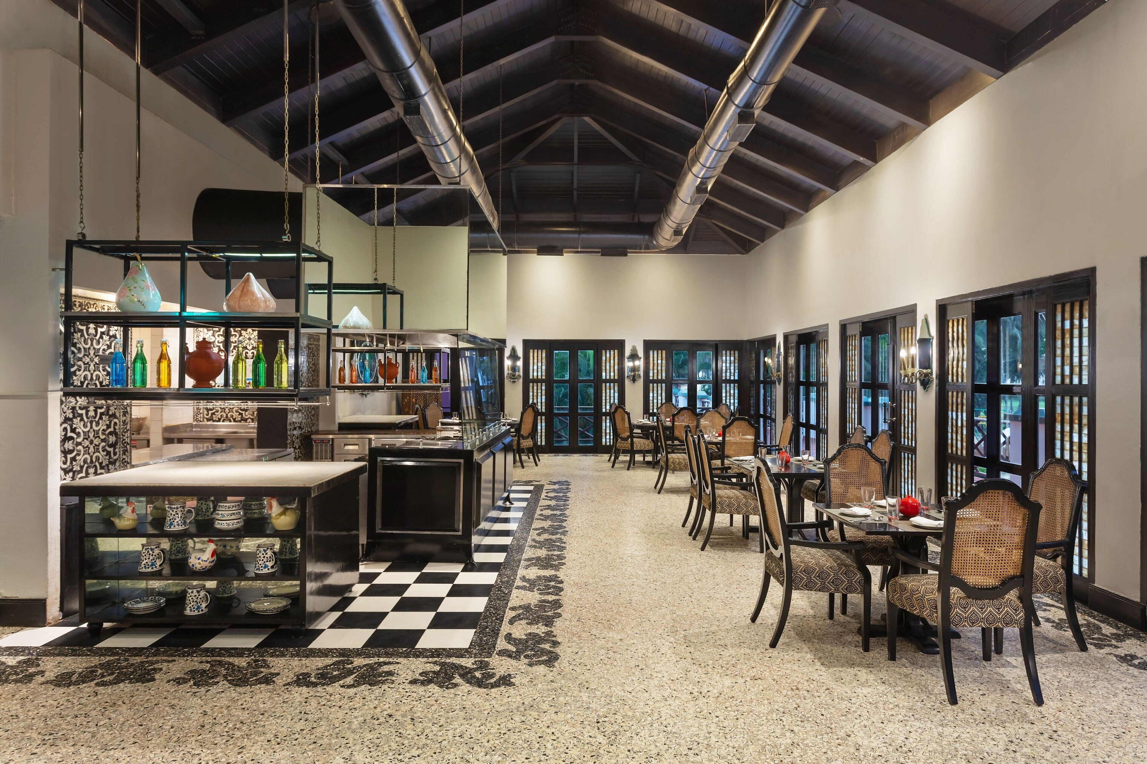 A spacious hotel lobby with a checkered floor, a central seating area with tables and chairs, and shelves displaying various decorative items.