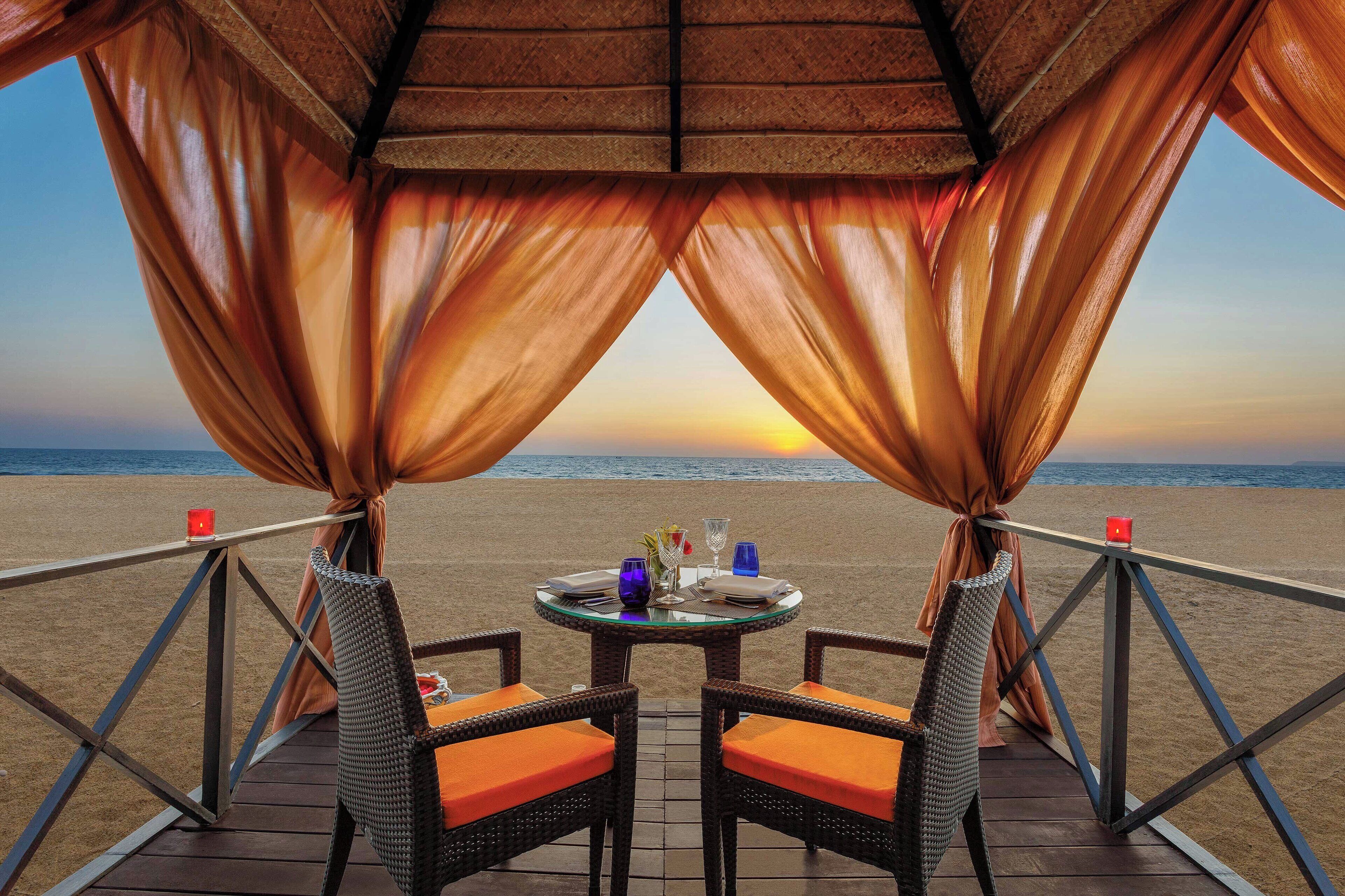 A dining table with chairs and a view of the beach at sunset.