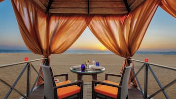 Una mesa de comedor con sillas y vista al mar al atardecer.