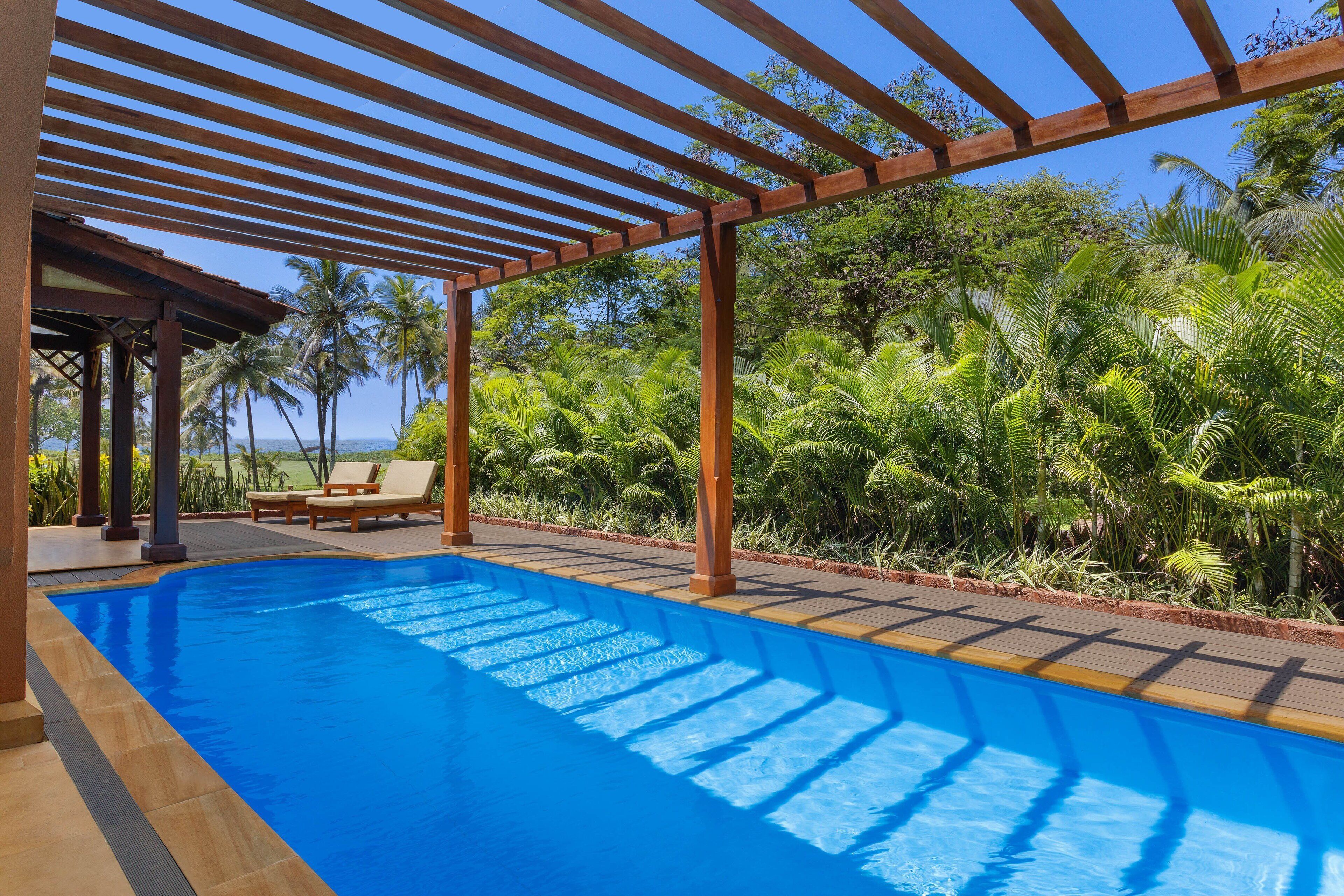 A swimming pool with wooden pergola overhead, surrounded by lush greenery and palm trees.